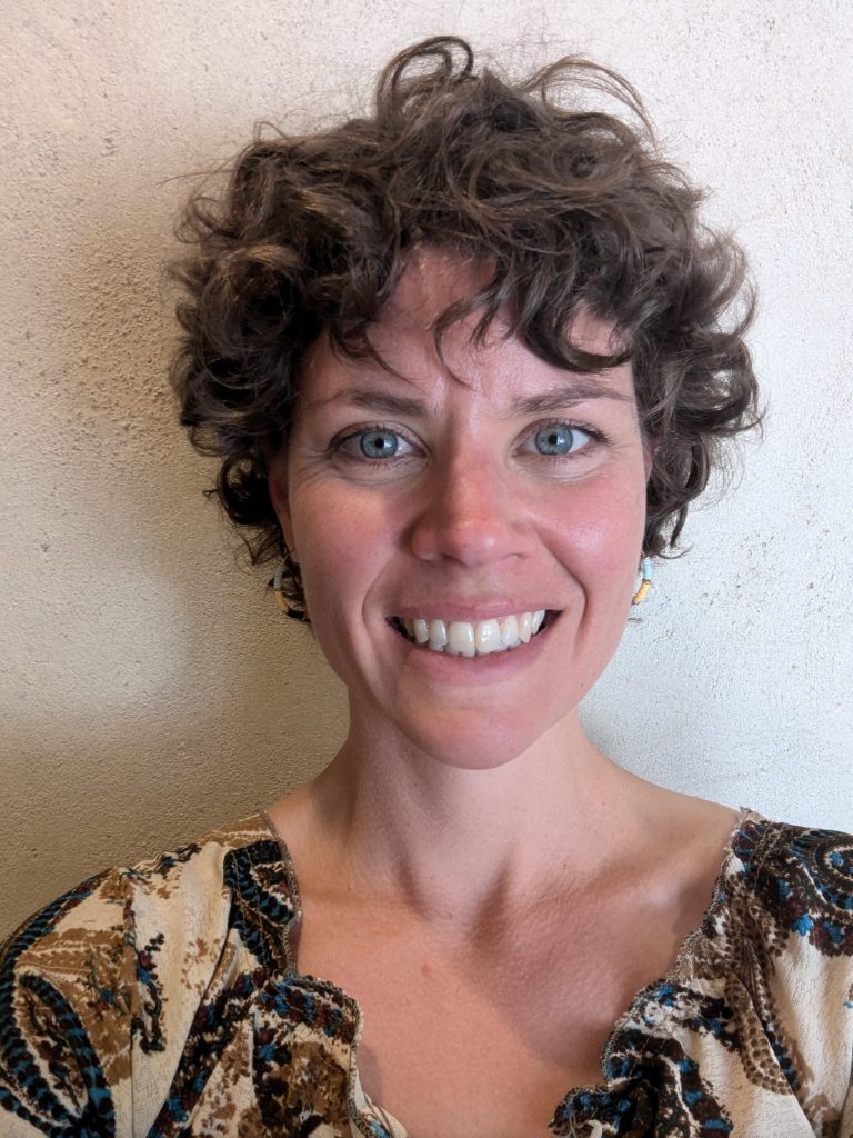 Smiling woman with curly hair and patterned blouse.