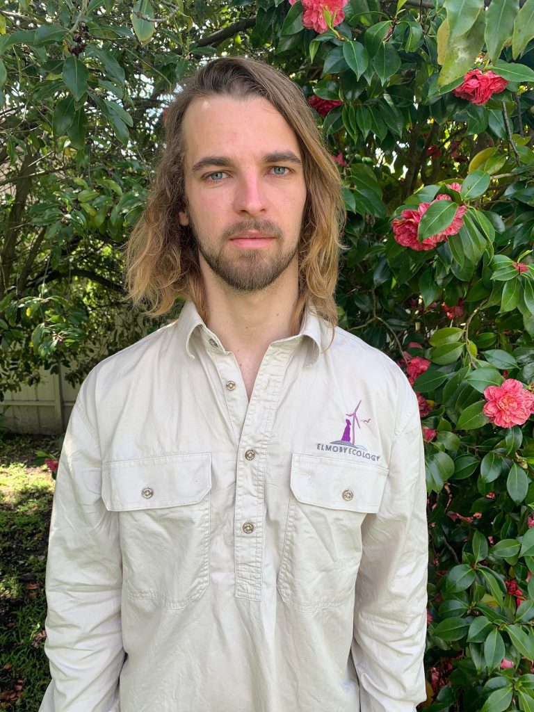 Person in garden wearing a beige shirt with logo.