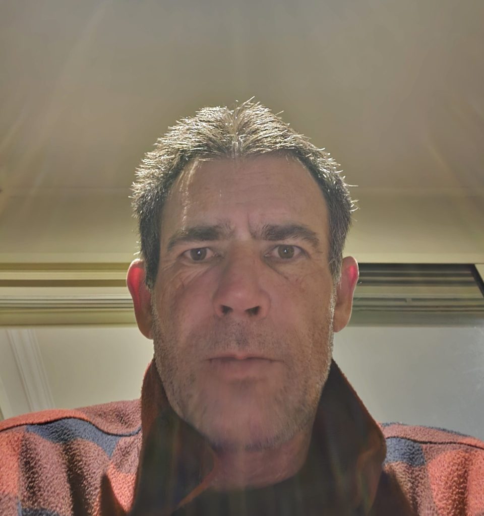 Man in red checkered jacket under bright light.