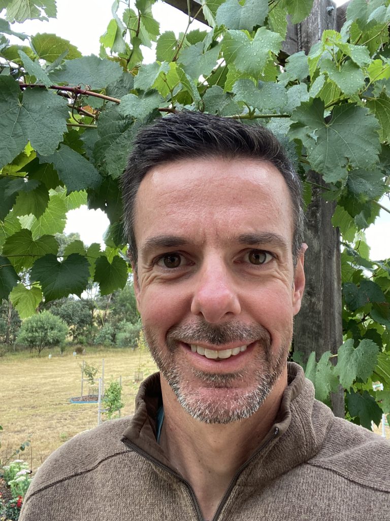 Smiling person in garden under grapevines.